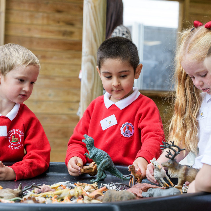 Young children exploring a tray of toy dinosaurs