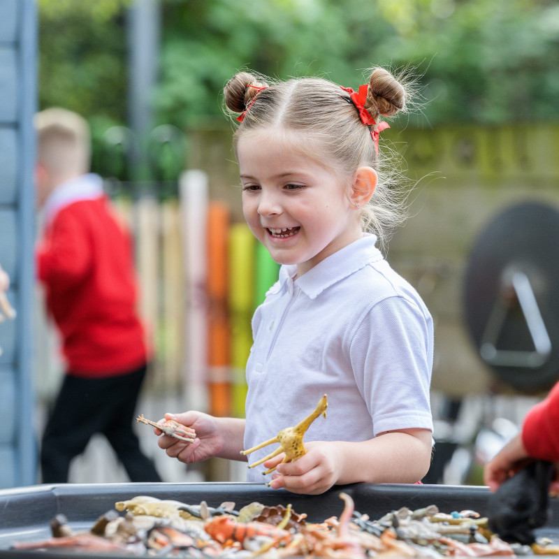 A smiling girl playing with toy dinosaurs outdoors