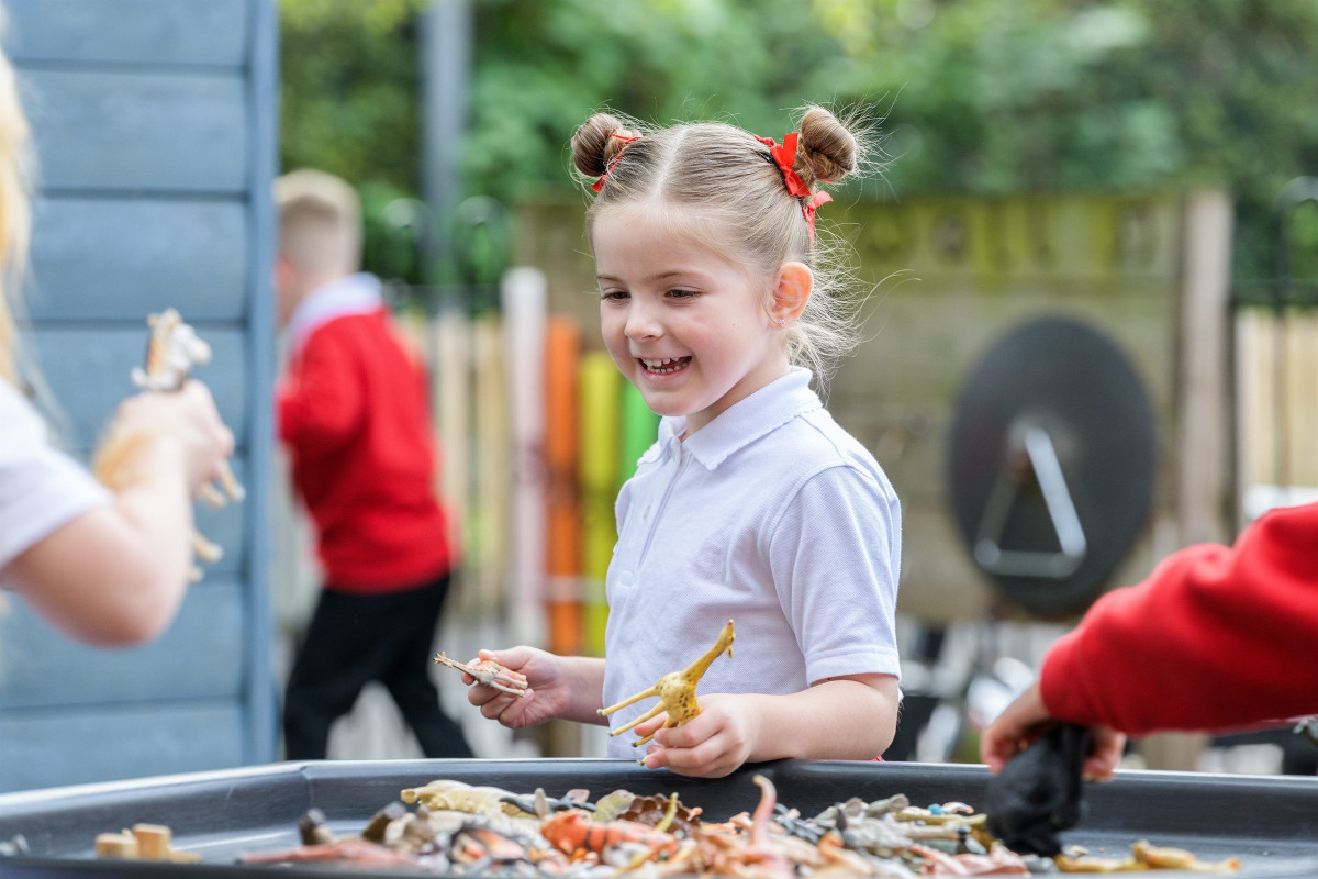 A smiling girl playing with toy dinosaurs outdoors