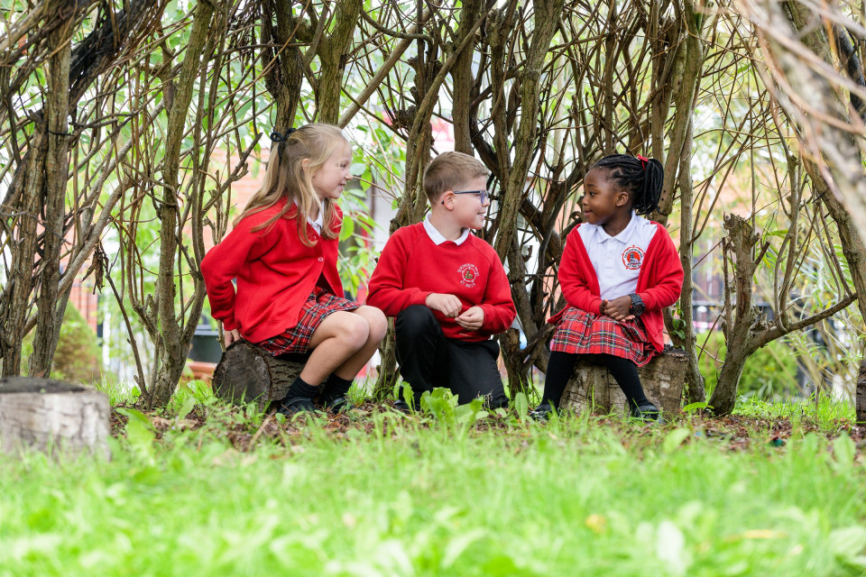Three children sitting together under the trees in the school grounds